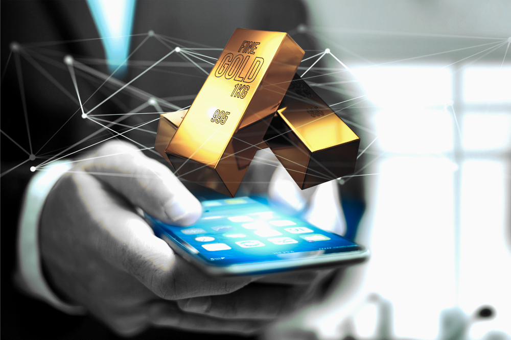 Widok złota w sztabkach lśniącego nad smartfonem trzymanym w ręku mężczyzny w garniturze